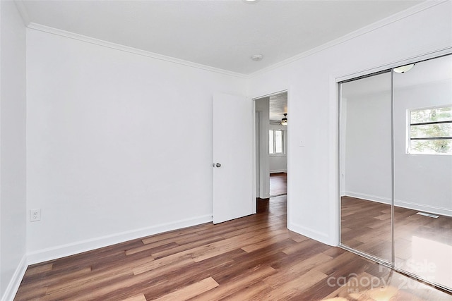 unfurnished bedroom with ornamental molding, a closet, baseboards, and wood finished floors