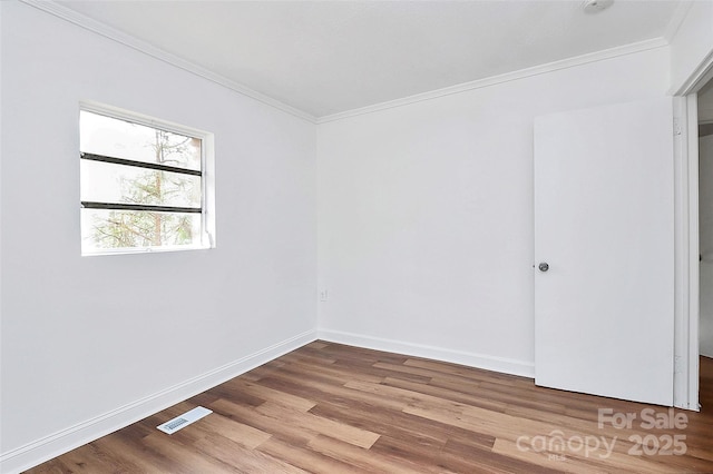 empty room featuring baseboards, wood finished floors, visible vents, and crown molding