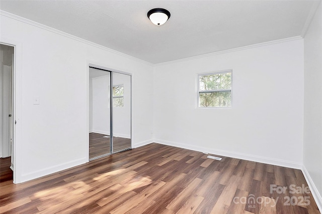 unfurnished bedroom featuring baseboards, a closet, wood finished floors, and crown molding