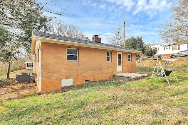 rear view of property featuring central AC unit, a chimney, crawl space, a yard, and brick siding