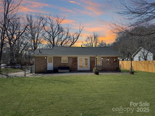 view of front of home featuring french doors, brick siding, a yard, a patio, and fence