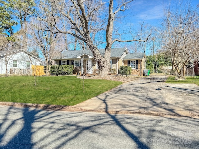 ranch-style home featuring driveway, fence, a front lawn, and brick siding