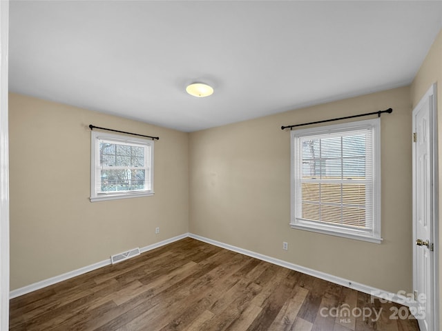 unfurnished room featuring wood finished floors, visible vents, and baseboards