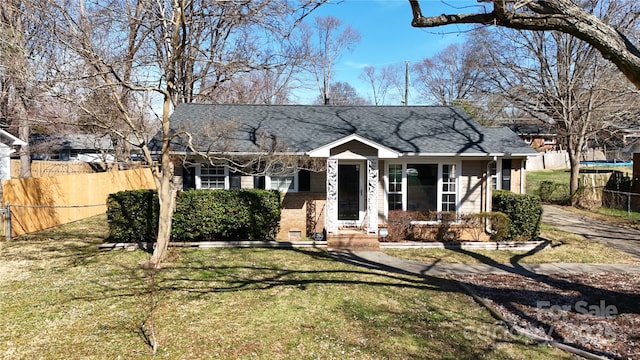 view of front of home with roof with shingles, a trampoline, a front yard, and fence