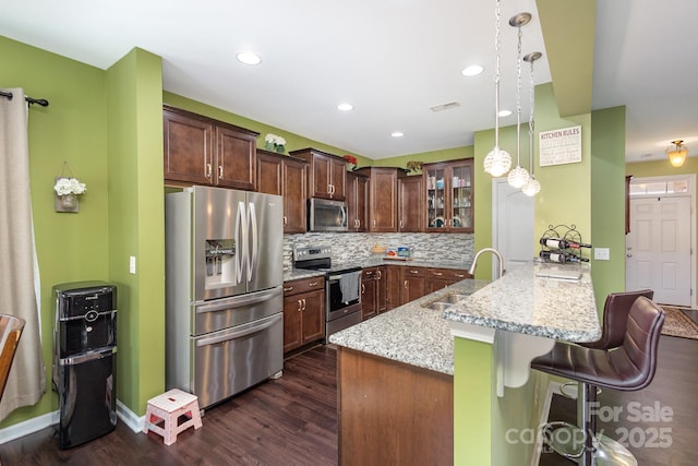 kitchen featuring a breakfast bar area, appliances with stainless steel finishes, a sink, light stone countertops, and a peninsula