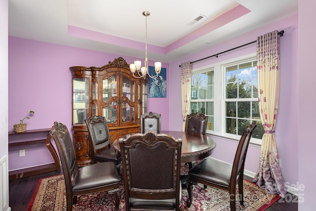 dining room featuring wood finished floors, a raised ceiling, visible vents, and baseboards