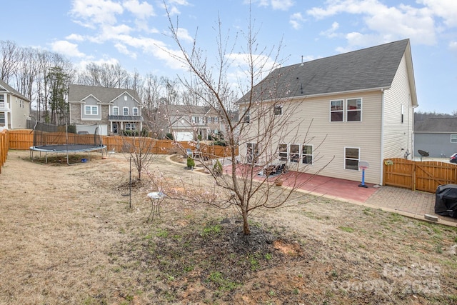 rear view of property with a fenced backyard, a trampoline, a residential view, and a patio