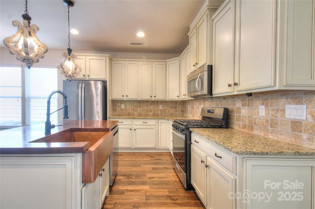 kitchen featuring light wood-style flooring, visible vents, decorative backsplash, pendant lighting, and appliances with stainless steel finishes