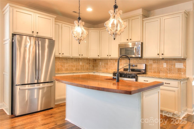 kitchen with stainless steel appliances, a kitchen island with sink, backsplash, wood finished floors, and wood counters