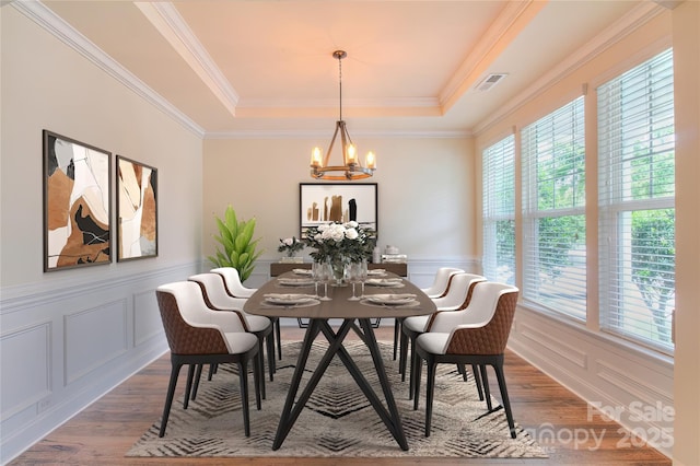 dining room with a tray ceiling, visible vents, an inviting chandelier, wood finished floors, and a decorative wall