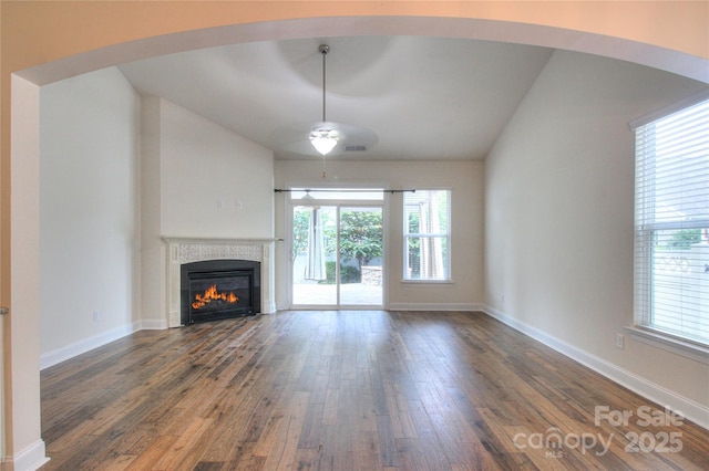 unfurnished living room featuring lofted ceiling, a tile fireplace, a ceiling fan, wood-type flooring, and baseboards
