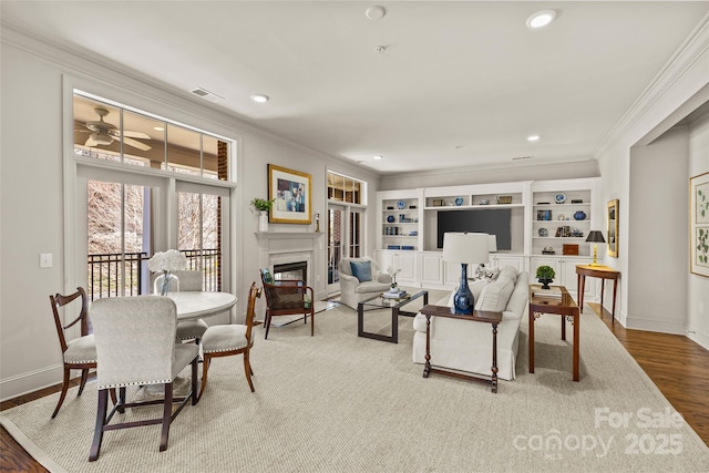 living room with ornamental molding, a glass covered fireplace, visible vents, and wood finished floors