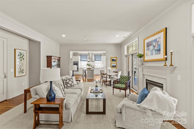 living room featuring recessed lighting, ornamental molding, a high end fireplace, light wood-style floors, and baseboards