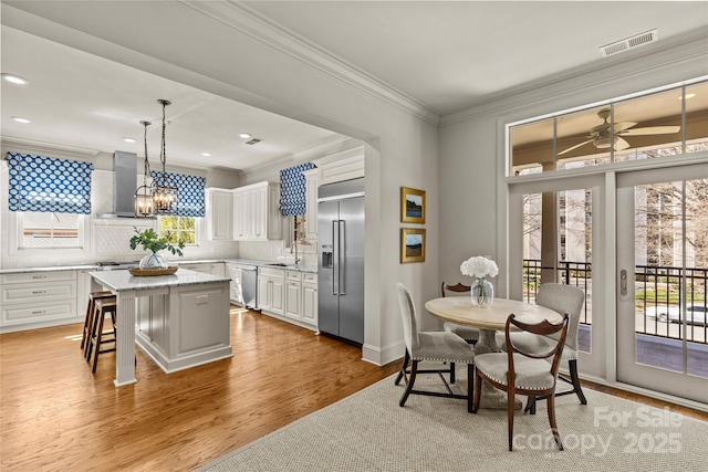 kitchen featuring a sink, visible vents, appliances with stainless steel finishes, wall chimney exhaust hood, and crown molding