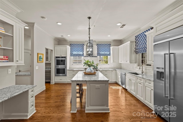 kitchen featuring white cabinets, a kitchen island, stainless steel appliances, crown molding, and a sink