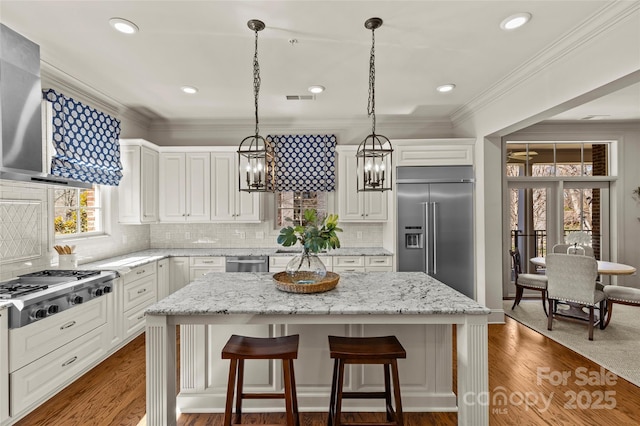 kitchen with stainless steel appliances, a kitchen island, wall chimney exhaust hood, a kitchen bar, and crown molding