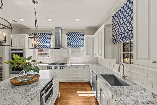 kitchen with stainless steel appliances, ornamental molding, a sink, wall chimney range hood, and light wood-type flooring