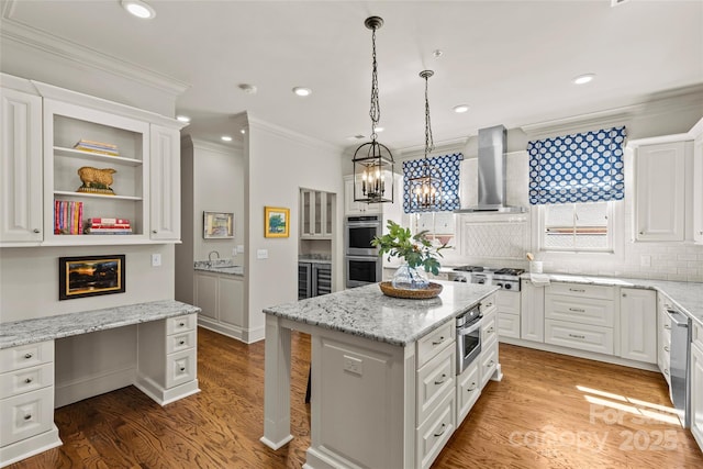 kitchen with crown molding, stainless steel appliances, built in study area, white cabinetry, and wall chimney range hood