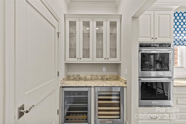 bar with double oven, beverage cooler, ornamental molding, and a dry bar