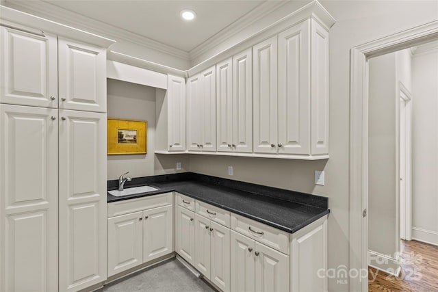 kitchen featuring dark countertops, white cabinets, a sink, and baseboards