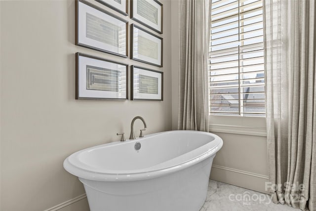 full bathroom featuring marble finish floor, a soaking tub, and baseboards