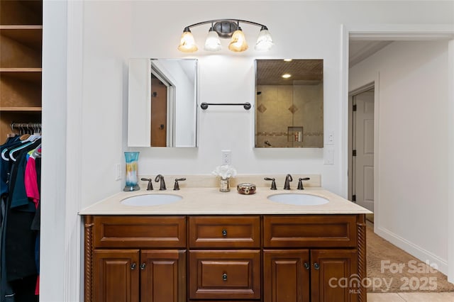 full bathroom featuring double vanity, a spacious closet, a tile shower, and a sink