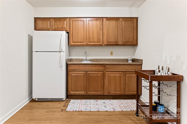 kitchen featuring a sink, baseboards, light wood-type flooring, freestanding refrigerator, and brown cabinets