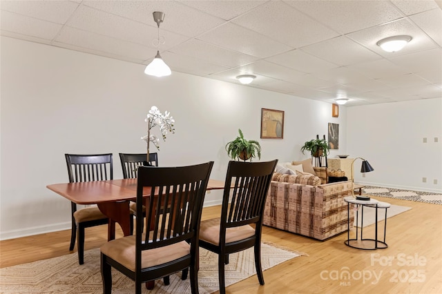 dining space with light wood-style flooring, baseboards, and a drop ceiling