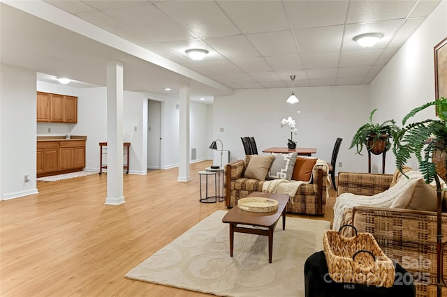 living room with baseboards, a drop ceiling, decorative columns, and light wood-style floors