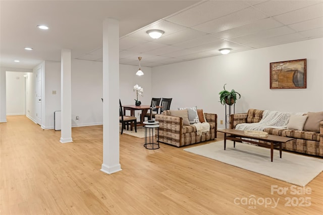 living area with light wood-type flooring, ornate columns, baseboards, and a drop ceiling