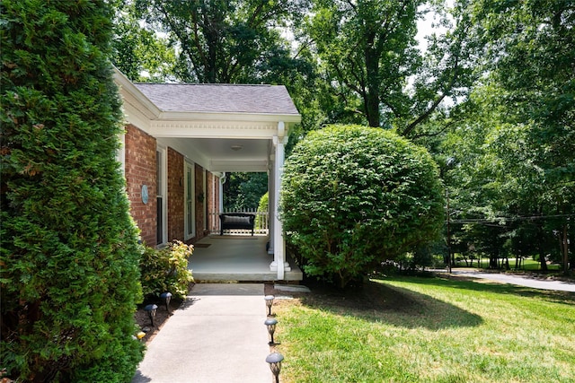 exterior space with covered porch, brick siding, a lawn, and a shingled roof