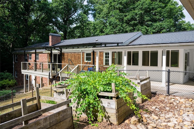 view of front of home with brick siding, fence, a garden, roof with shingles, and a chimney