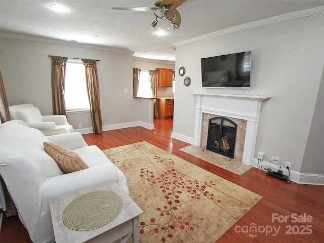 living room featuring crown molding, a fireplace, baseboards, and wood finished floors