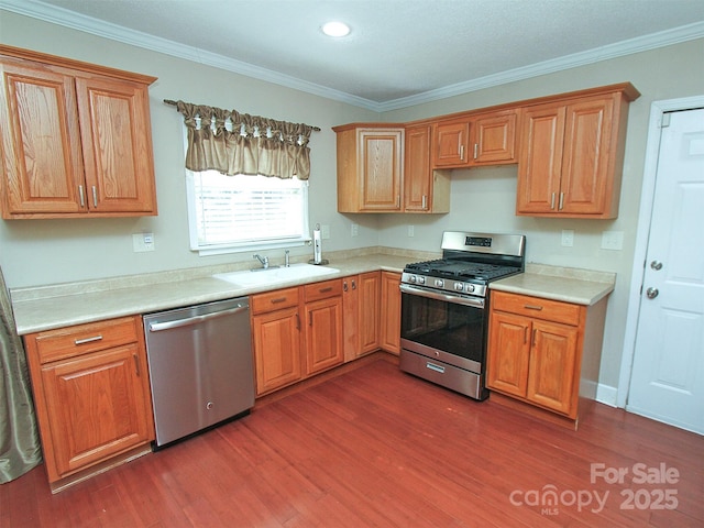 kitchen featuring dark wood finished floors, crown molding, light countertops, appliances with stainless steel finishes, and a sink