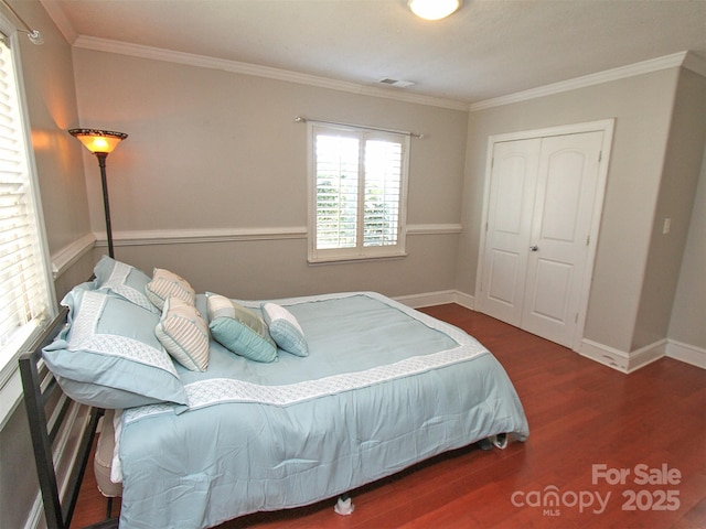 bedroom with wood finished floors, visible vents, baseboards, a closet, and crown molding