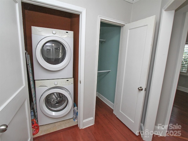 clothes washing area featuring laundry area, baseboards, stacked washer / dryer, and wood finished floors