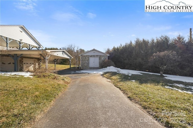 exterior space with aphalt driveway, a storage shed, an outdoor structure, a carport, and a front lawn