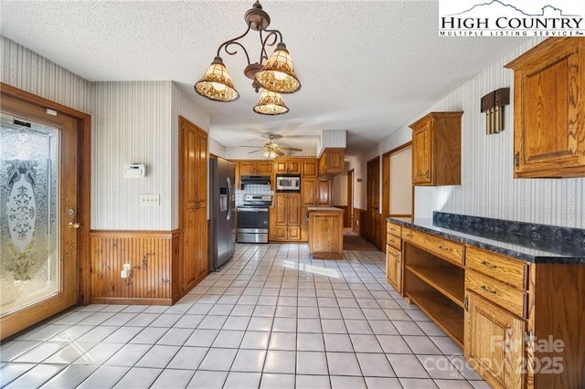 kitchen with appliances with stainless steel finishes, brown cabinetry, wainscoting, a textured ceiling, and wallpapered walls