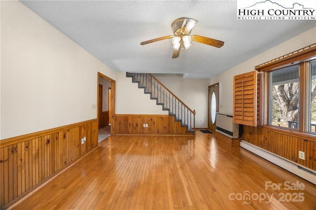 interior space featuring wooden walls, wainscoting, light wood-style flooring, stairway, and baseboard heating