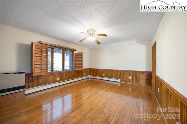 spare room featuring a baseboard radiator, wood-type flooring, wainscoting, and a textured ceiling