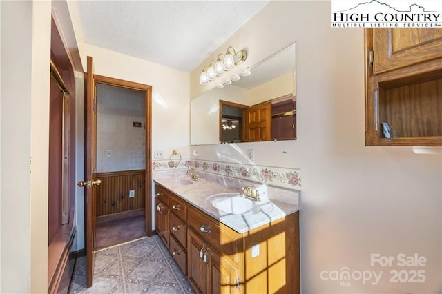 bathroom with a textured ceiling, wooden walls, a sink, wainscoting, and double vanity