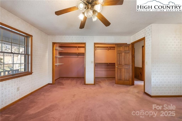 unfurnished bedroom with light carpet, wallpapered walls, baseboards, and multiple closets