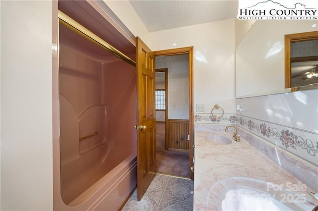 bathroom with a wainscoted wall, double vanity, a textured ceiling, and a sink