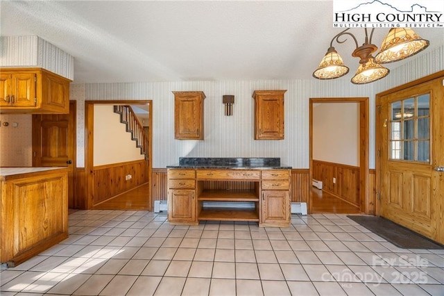 kitchen with wallpapered walls, a wainscoted wall, open shelves, brown cabinetry, and an inviting chandelier