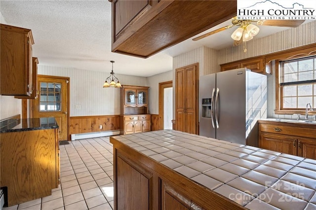 kitchen with wallpapered walls, wainscoting, stainless steel fridge with ice dispenser, a baseboard radiator, and brown cabinets