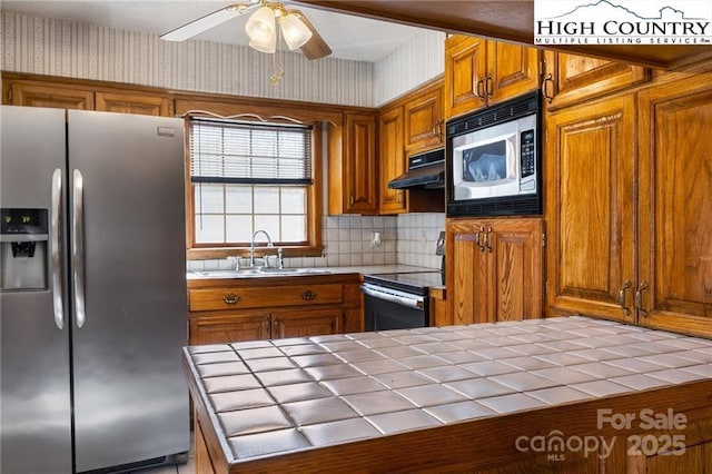 kitchen featuring under cabinet range hood, wallpapered walls, appliances with stainless steel finishes, and tile counters