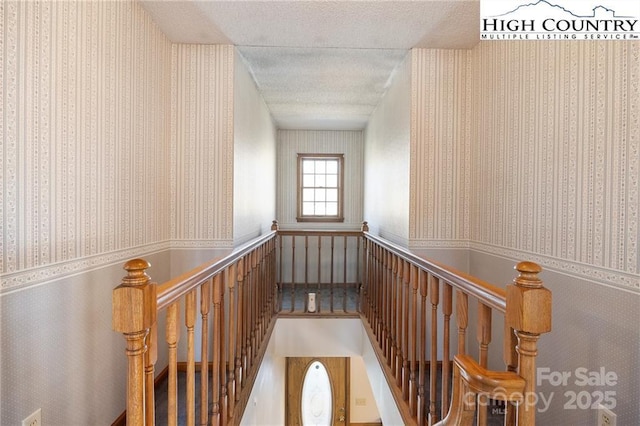 corridor featuring a textured ceiling, an upstairs landing, and wallpapered walls