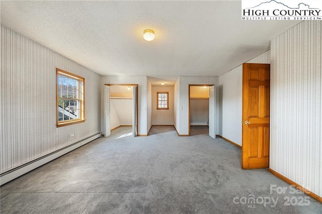 unfurnished bedroom featuring wallpapered walls, baseboards, a baseboard radiator, a textured ceiling, and multiple closets