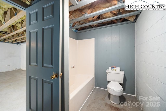 full bathroom with concrete flooring, concrete block wall, toilet, and a bathing tub