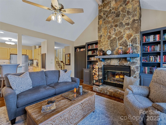 living room featuring ceiling fan, a stone fireplace, light wood-style flooring, and stairs